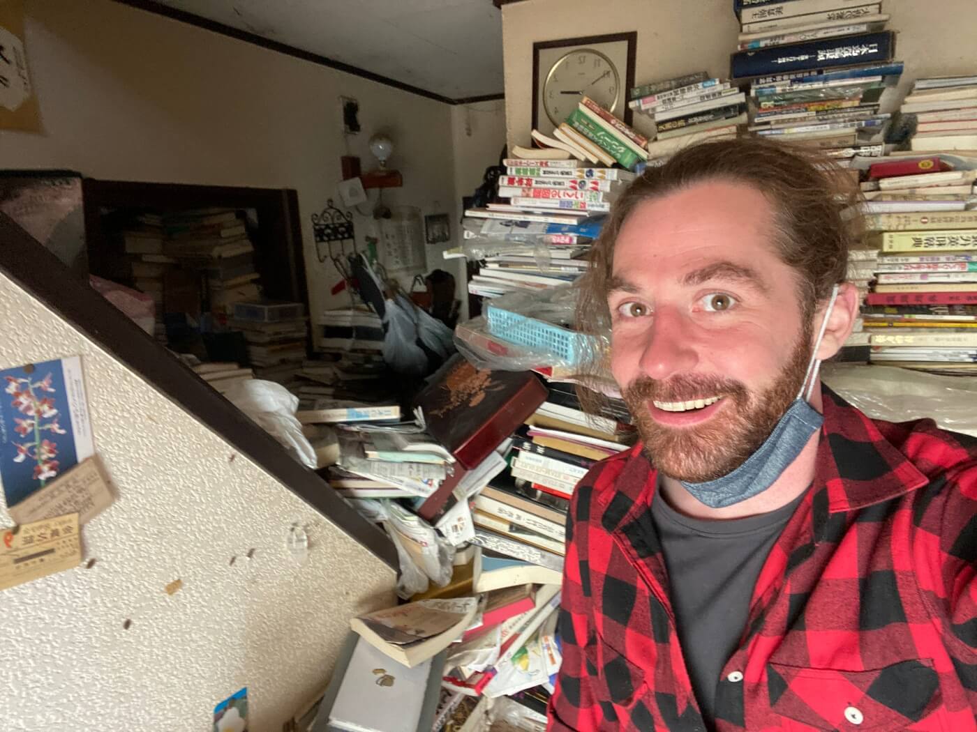 Matt Ketchum of Akiyaz wearing a red and black checkered shirt in a hoarder house full of books in Japan.